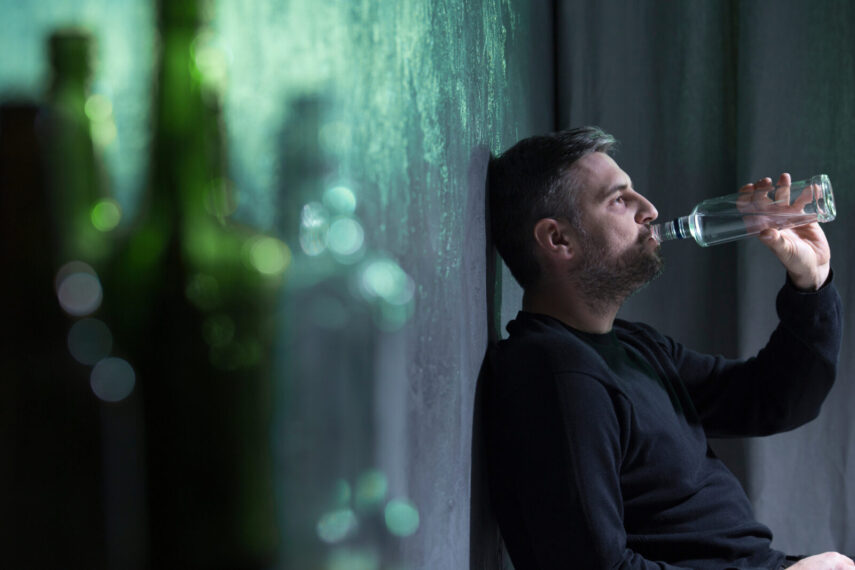 Man wearing black clothes drinking alcohol from transparent bottle alone