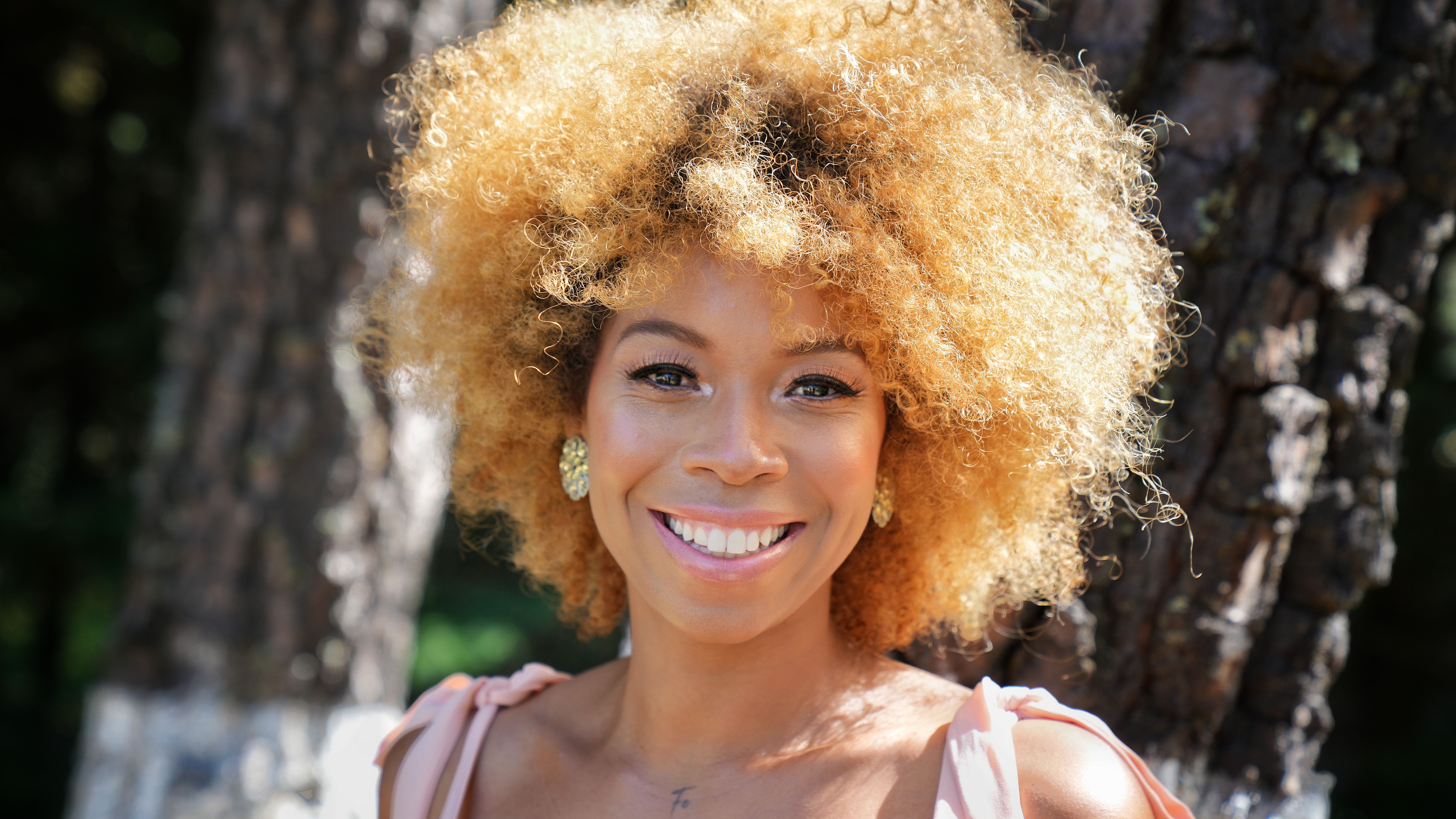Portrait of a woman with curly hair smiling naturally outdoors in a sunny park, radiating authentic confidence