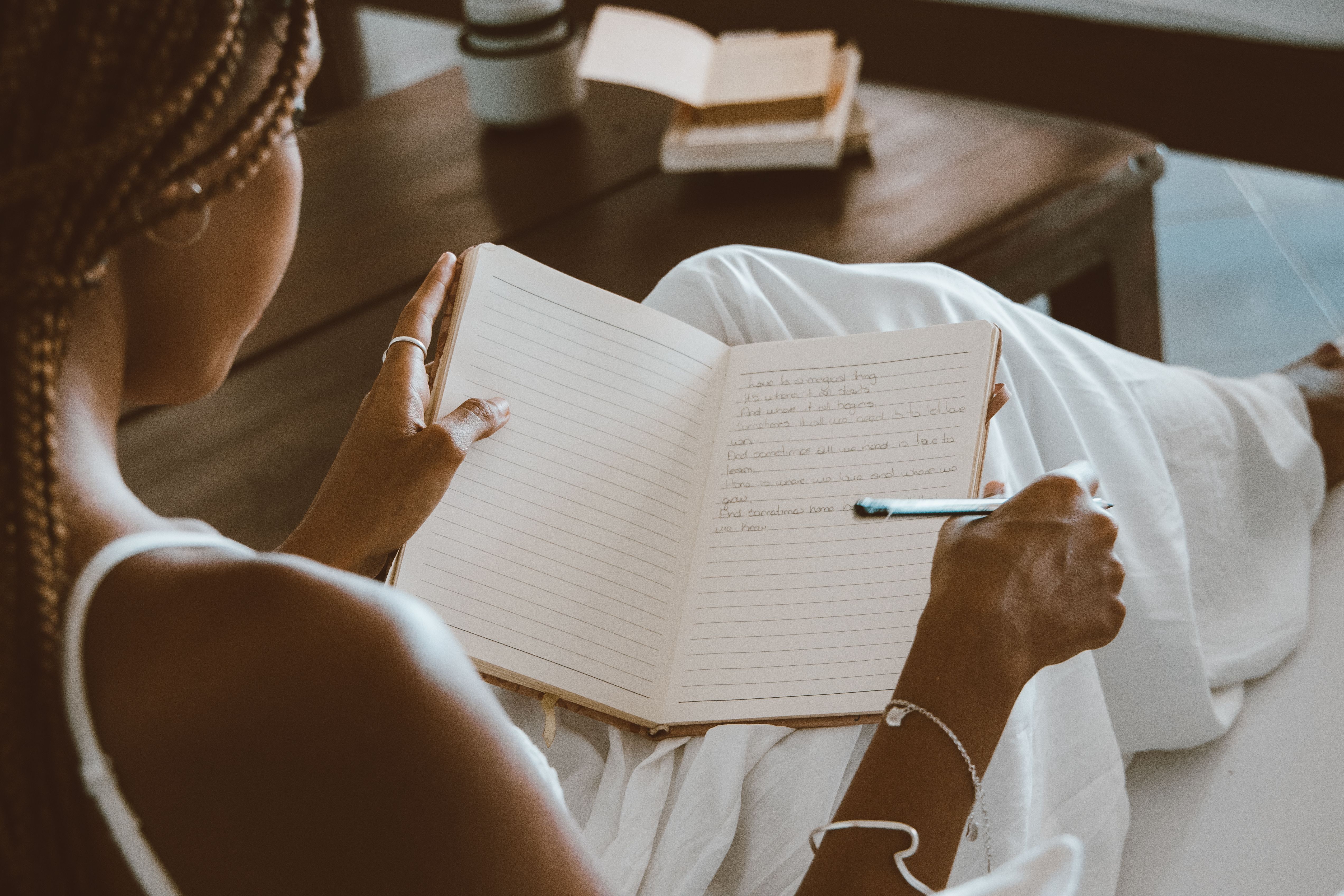 A woman writing in a notebook in a calm room with natural light, practicing journaling to build self-worth