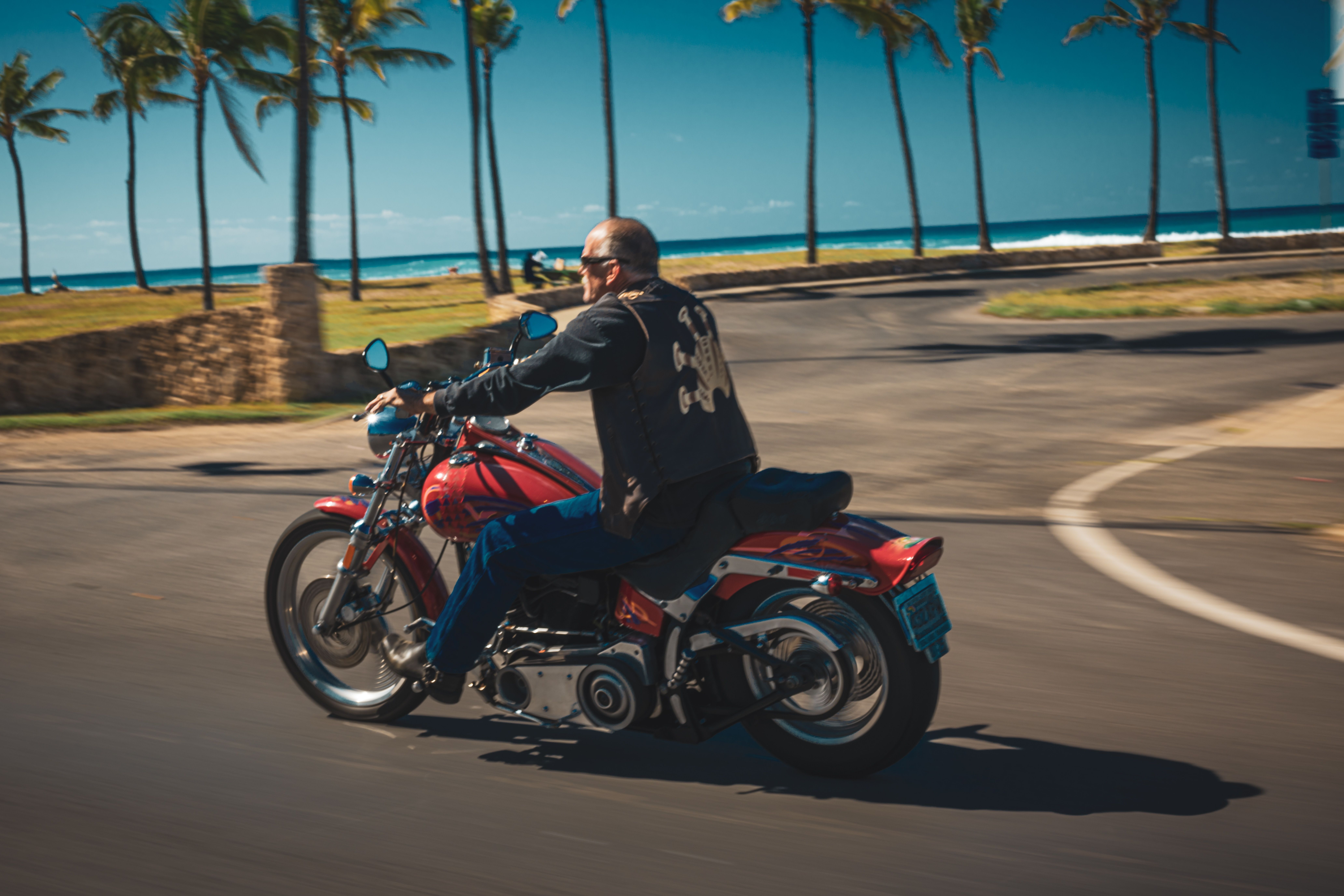 Biker riding a red motorcycle along a tropical palm-lined coast in summer