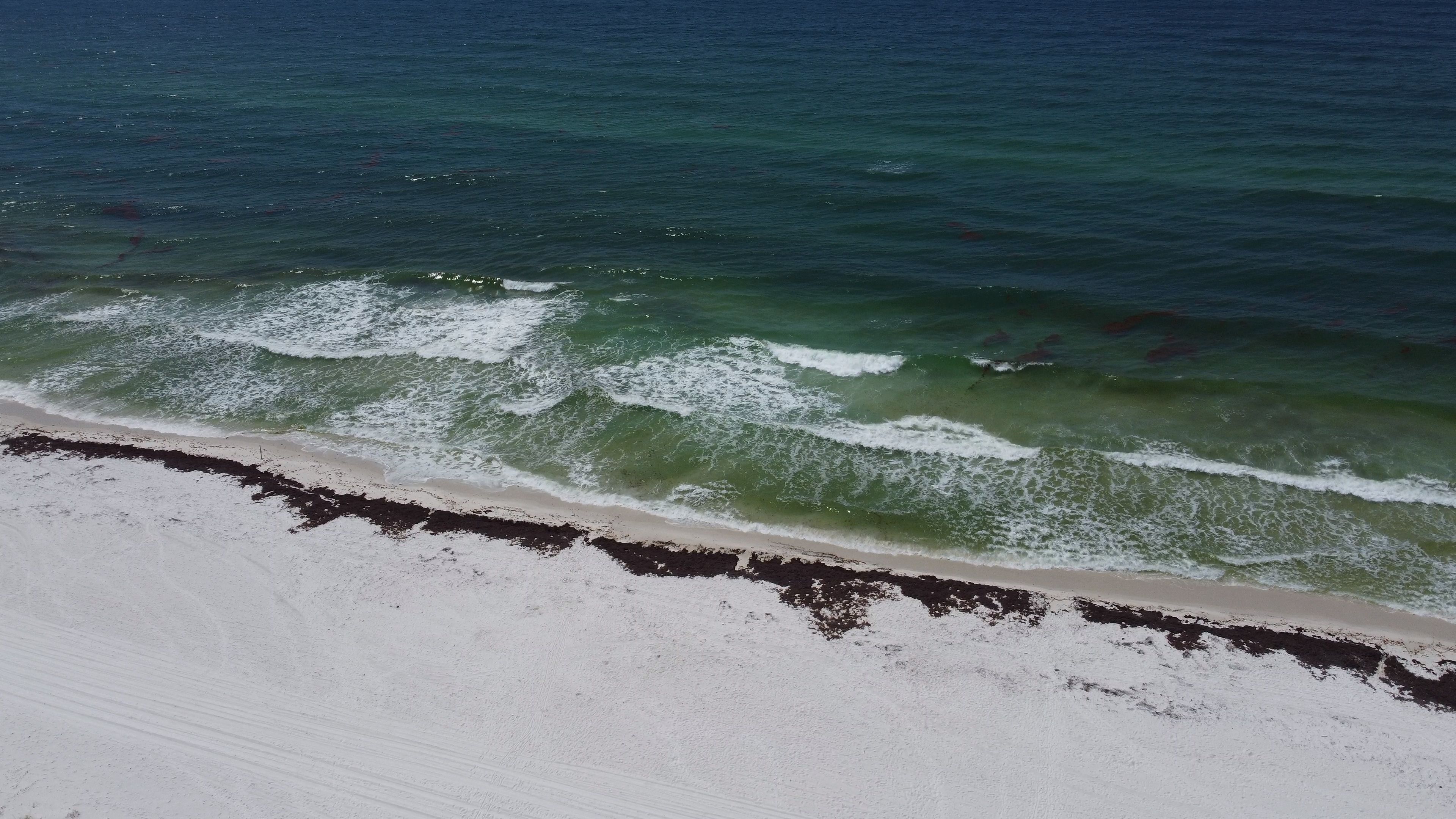 Aerial view of Pensacola Beach with waves crashing on white sand under a summer sky