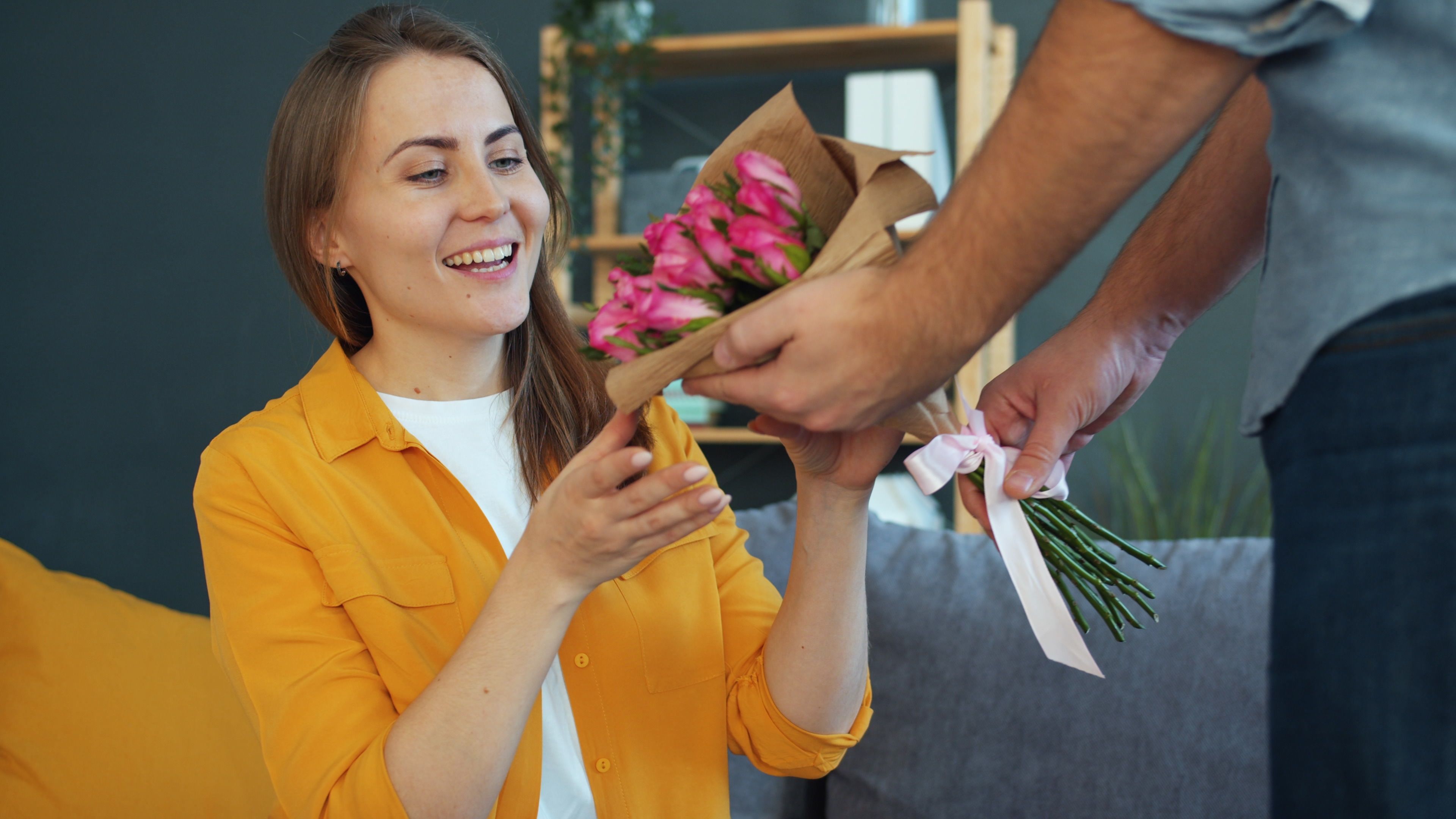 A woman happily receiving a bouquet of pink flowers indoors, feeling valued and appreciated