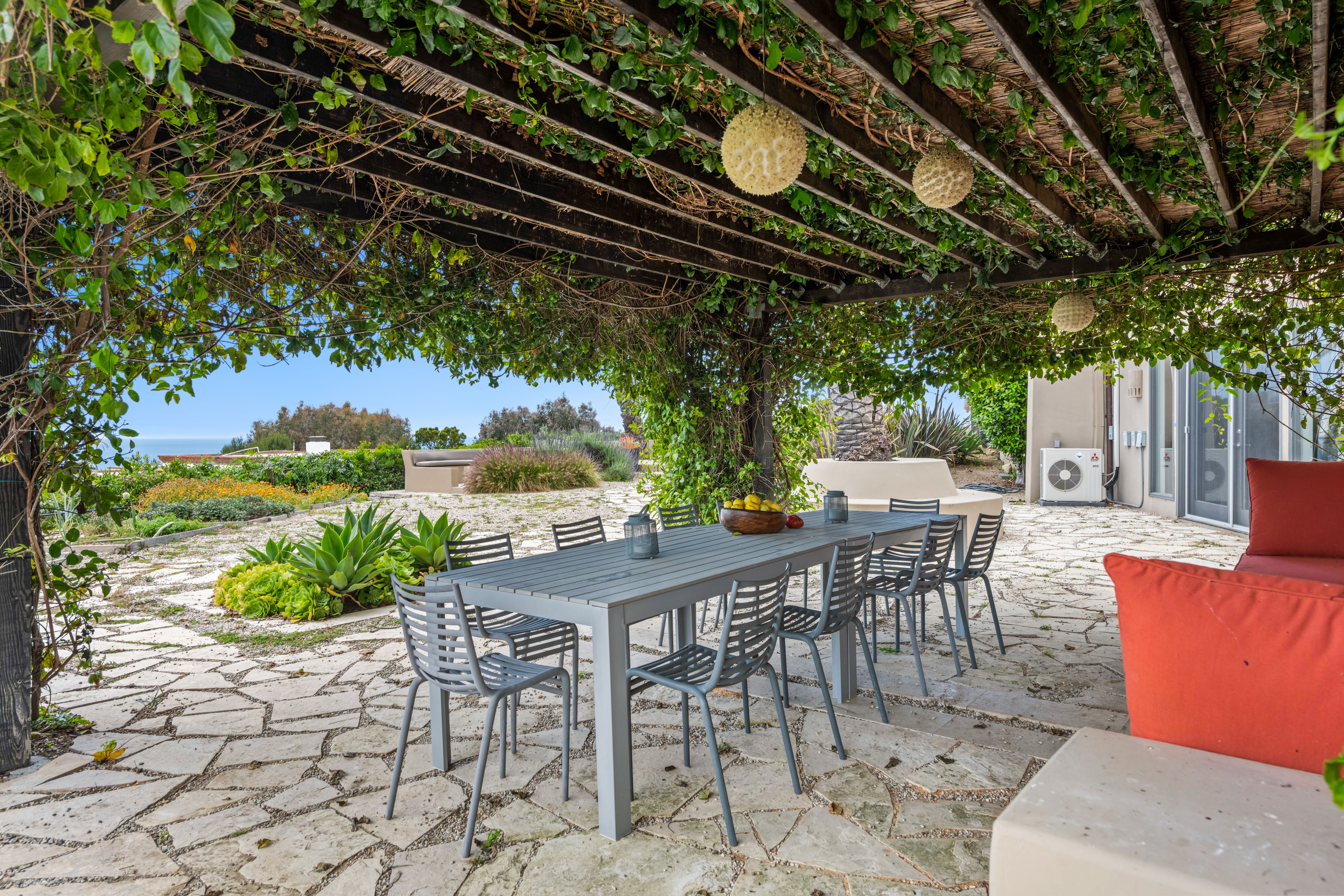 Garden dining patio beneath a vine-covered pergola with an ocean view
